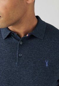 Navy-blaues Poloshirt aus strukturiertem Stoff, mit einem zwei-knopf Plastron und einem bunten gestreiften Kragenfutter. Kleines gesticktes Logo auf der Brust.