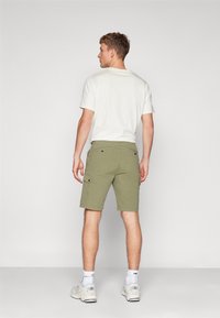 Pantaloni cargo verde oliva con tasche laterali, abbinati a una t-shirt bianca a collo rotondo. Il modello è in piedi con la schiena rivolta verso la fotocamera.