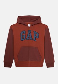 Haut à capuche zippé rouille et rouge foncé avec poches avant et logo "GAP" bleu sur la poitrine.