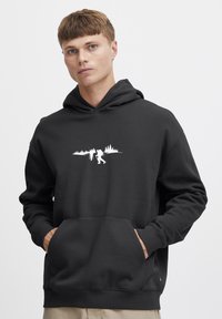 Sudadera gris oscuro con bolsillo frontal; presenta un gráfico blanco de un excursionista y árboles en el pecho; textura suave y ajuste estándar.