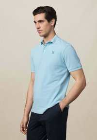 Polo shirt azzurro chiaro con logo di marca sul petto, maniche corte e colletto. Tessuto morbido con design aderente.