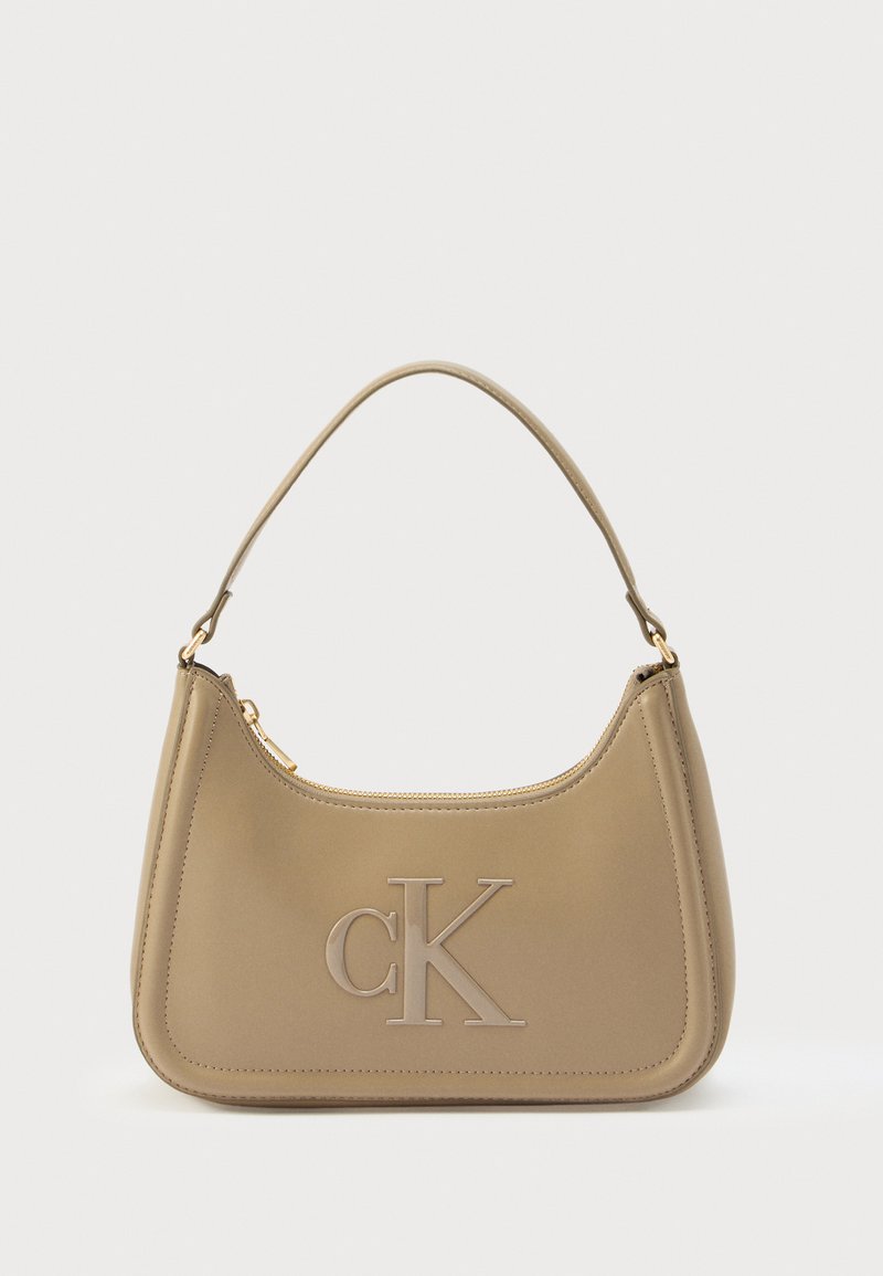 Calvin Klein-handväska i taupefärgat läder med en mjuk textur, rundad form, präglad "CK"-logotyp och en enkel axelrem. Dragkedja på toppen.