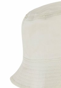 Cream-colored cotton bucket hat featuring a wide brim, textured fabric, and visible stitching along the crown and brim edges.