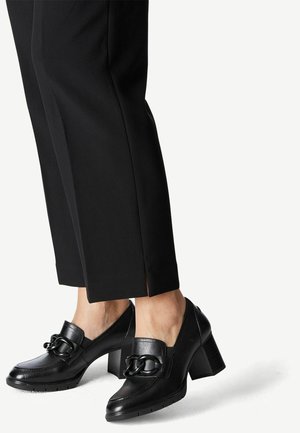 Black heeled loafers feature a smooth leather upper, a wide strap with a chain accent, and a textured block heel. Pairing with black trousers.