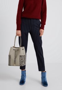 Šedá kabela na rameno s akcenty v hadím vzoru, spárovaná s námořnickými kalhotami s jemným proužkem a modrými sametovými kotníkovými botami. Pletený červený svetr.