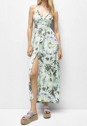 Femme portant une robe maxi à effet tie-dye à col licou avec une fente haute et des sandales à plateforme sur un fond uni.