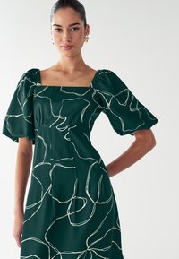 Roheline puff-sleeve kleit, millel on ruudukujuline kaelus, voolav kangas valge abstraktse joontega mustriga ning figureeriv vöökoht.