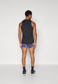 Schwarzes ärmelloses Tanktop mit figurbetontem Design; getragen mit mehrfarbigen gemusterten Shorts. Auch schwarze Sportschuhe und Socken sind sichtbar.
