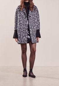 Grijze jas met luipaardprint, een losse pasvorm, een oversized kraag en twee voorzakken. Draagt over een zwart topje en een zwarte leren rok.