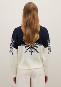 Pull tricoté bleu marine et crème avec motif flocon de neige sur les épaules et les manches. Ourlet et poignets côtelés, coupe décontractée.