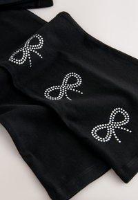 Tessuto nero con tre grandi fiocchi decorati con strass. Texture liscia, con una forma sagomata e bordi puliti.