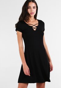 Czarna sukienka z krótkim rękawem o dopasowanej górze i rozkloszowanej spódnicy, z dekoltem w kształcie klucza i skrzyżowanymi detalami oraz gładką teksturą materiału.