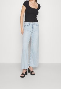 Černé přiléhavé tričko s krátkým rukávem, v kombinaci s světle modrými širokými džíny a černými sandály na blokovém podpatku. Jednoduchý design, ležérní vzhled.