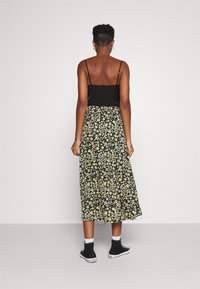 Camisola nera con spalline sottili abbinata a una gonna midi floreale in nero e giallo. La modella indossa sneaker alte nere e calze bianche.
