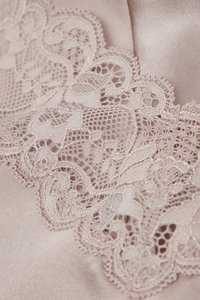 Silkeblødt lyserødt stof med detaljeret beige blondekant med blomsterprint og bølgede kanter.