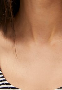 Primer plano de un área del cuello con un tono de piel claro, que presenta cabello liso y oscuro, y un tejido a rayas en el fondo, creando un efecto de capas.