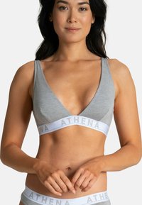 Bralette en coton doux gris avec un décolleté en V profond, des larges bretelles et une bande blanche portant le texte "ATHENA". Design léger et sans couture.