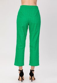 Pantalons verts courts avec un design perforé et une texture lisse, associés à des sandales à talons noirs.