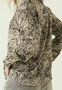 Košile s dlouhým rukávem vyrobená z lehké látky s béžovým, černým a zeleným abstraktním vzorem; má volný střih a ohrnuté rukávy.