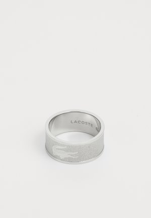Bague en argent avec une finition mate, dotée d'une surface texturée et du logo Lacoste gravé. Forme ronde avec une large bande.