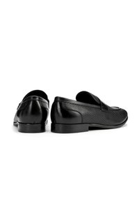 Mocasines negros de cuero texturizado, con costura decorativa y un tacón liso. Presentan una punta redondeada y un diseño fácil de poner.