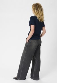 T-shirt navy a maniche corte abbinato a jeans grigi scuri a gamba larga e scarpe nere a punta, visto da dietro, evidenziando la vestibilità rilassata e lo stile casual.