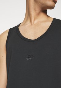 Melnas kokvilnas topiņš ar apaļu kakla izgriezumu. Uz krūtīm ir neliels, tonāls izšūts Nike logo. Gluda tekstūra, sportisks piegriezums.