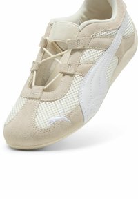 Zapatilla deportiva en beige y blanco con parte superior de ante y malla, que presenta un diseño con cordones y un cuello acolchado, suela de goma ligera.