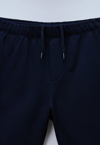 Σκούρες μπλε φόρμες από βαμβάκι, με ελαστική μέση και κορδόνια καθώς και μπροστινή τσέπη. Λείο ύφασμα, μίνιμαλ σχεδιασμός.