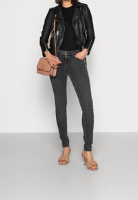 Chaqueta de motorista de cuero negro, blusa negra, jeans ajustados gris oscuro y bolso beige; sandalias de tacón beige con acentos texturizados.