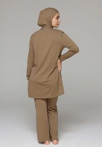 Beige bescheiden zwemset bestaande uit een lange top met een hoge hals en bijpassende broek. De stof lijkt glad en aansluitend met lange mouwen.