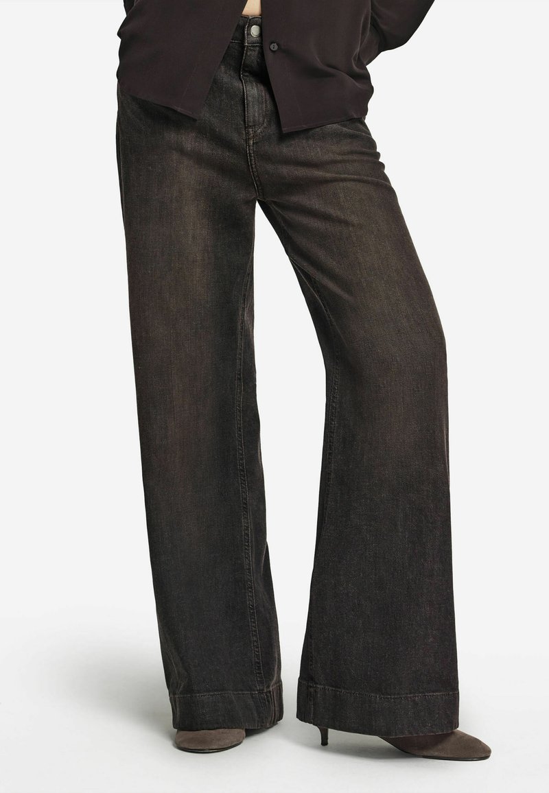 Jean en denim noir à jambes larges avec une texture légèrement délavée, doté d'une braguette traditionnelle à boutons et zip, et d'un ourlet fini de manière lisse.