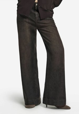 Schwarze Jeans mit weitem Bein und leicht verwaschener Textur, ausgestattet mit traditionellem Knopf- und Reißverschluss sowie einem sauberen Saumabschluss.