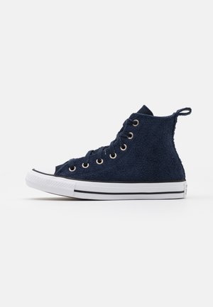 Baskets montantes bleu marine avec texture éponge, semelle en caoutchouc blanche avec une bande noire, œillets métalliques et languette au talon.