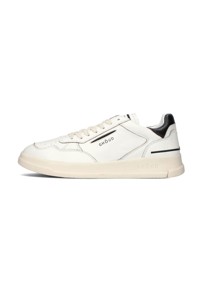 Witte leren sneakers met beige rubberen zool, zwarte hielaccent, minimalistisch design, gestikte details en merklogo aan de zijkant.
