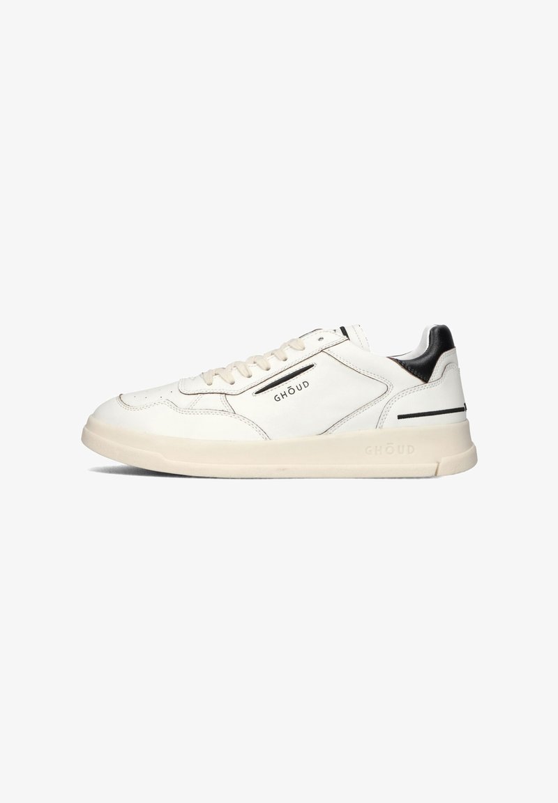 Witte leren sneakers met beige rubberen zool, zwarte hielaccent, minimalistisch design, gestikte details en merklogo aan de zijkant.