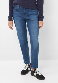 Jeans in denim blu con taglio dritto, dotati di tasche frontali, cuciture sottili e una texture liscia e leggermente elastica. Abbinati a sneakers nere.