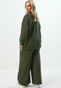 Olivgrön, oversized sweatshirt med ribbade ärmslut och nederkant, kombinerad med vida byxor. Slät textur, avslappnad passform och minimalistisk design.