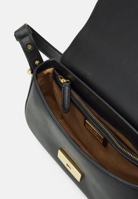 Mustanköynnöksinen käsilaukku, jossa on sileä pinta, kultaiset yksityiskohdat ja vetoketjullinen sisätasku. Vuorattu ruskealla kankaalla. Suorakulmainen muoto.