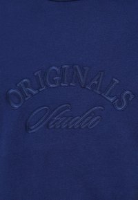 Sweat à capuche bleu marine avec des logos brodés "ORIGINALS" et "Studio" dans une couleur tonale. Texture douce et coupe standard.