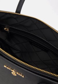 Interieur van een zwarte leren handtas met een gequilt patroon, gouden rits en logo-detail. Gladde textuur met een georganiseerde indeling.