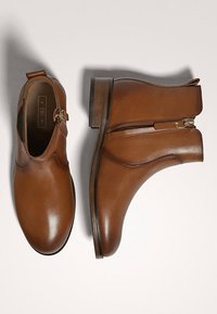 Brązowe skórzane botki za kostkę z bocznymi zamkami i podwyższoną piętą. Gładka tekstura i zaokrąglony design noska z delikatnymi detalami szycia.