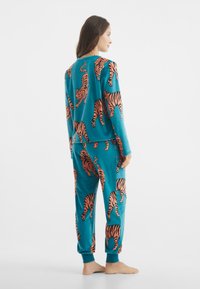 Conjunto de pijama turquesa con un estampado de tigres en toda la prenda en color naranja. Tejido suave con un corte relajado, mangas largas y cinturilla elástica.