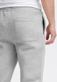 Graue Baumwoll-Jogginghosen mit glatter Textur, mit einer Gesäßtasche und seitlichen Nahttaschen. Elastischer Bund oben sichtbar.