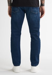 Jeans de mezclilla azul con corte recto, que cuentan con bolsillos traseros y detalles de costura, combinados con zapatillas blancas.