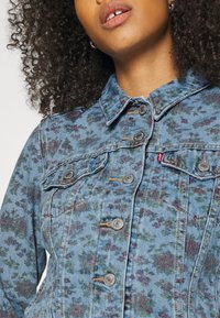 Denimjakke med blomster mønster i blå og grønne nuancer, med metal knapper og klassisk krave design. Teksturert stof finish.