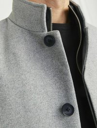 Grauer Wollmantel mit hohem Kragen, ausgestattet mit schwarzen Knöpfen und einem sichtbaren Reißverschluss. Strukturierter Stoff mit einer weichen, glatten Oberfläche.