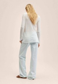 Top bianco a maniche lunghe con un design fluido, abbinato a pantaloni larghi blu chiaro. Tessuto morbido con una vestibilità rilassata, indossato con sandali marroni.