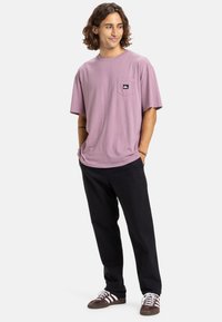 Svetlofialová bavlnená tričko s krátkymi rukávmi a náprsnou vreckom, skombinované s čiernymi nohavicami a hnedými teniskami s bielymi akcentmi.