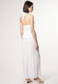 Witte halter peplumtop gecombineerd met losse witte broeken. Glad materiaal, ontspannen pasvorm en een strikdetail op de rug verbeteren het totale ontwerp.